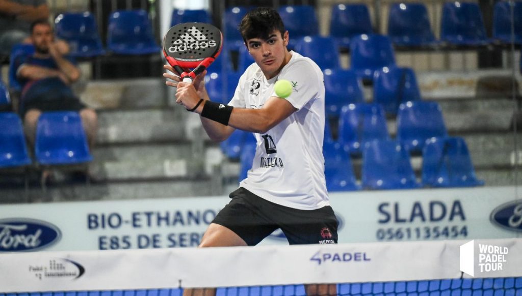 Padel player lunging for a low volley on a sand-dressed artificial turf court, wearing padel-specific court shoes